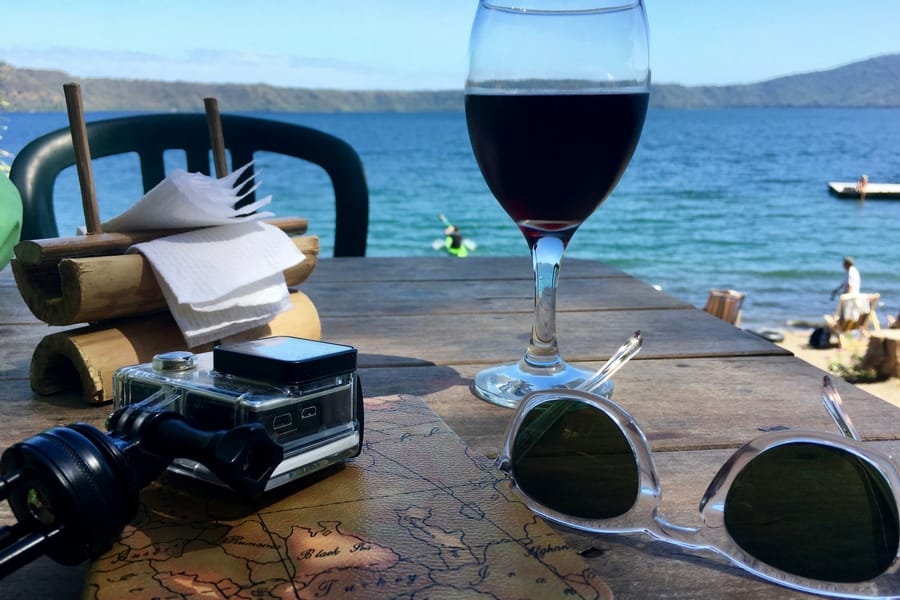 Image of the view of Laguna de Apoyo from San Simian Eco-Lodge including a glass of wine, GoPro, and sunglasses.