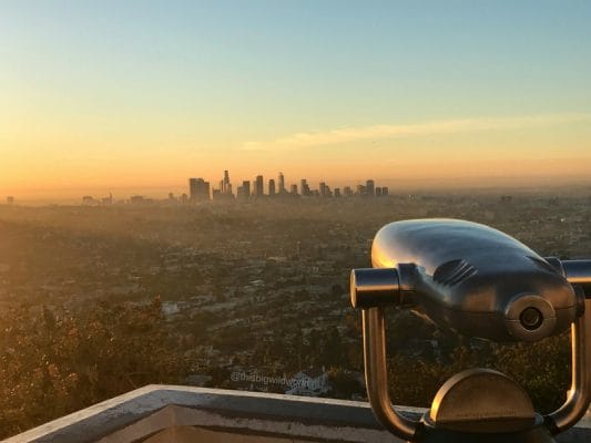 Image of downtown LA from Griffith Observatory at Sunrise in LA. The sky is bright pink and yellow.