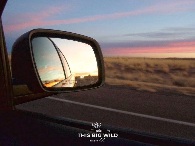 Image of rearview mirror with colorful pink and blue sunset as we drove through Arizona on our Los Angeles to Denver road trip.