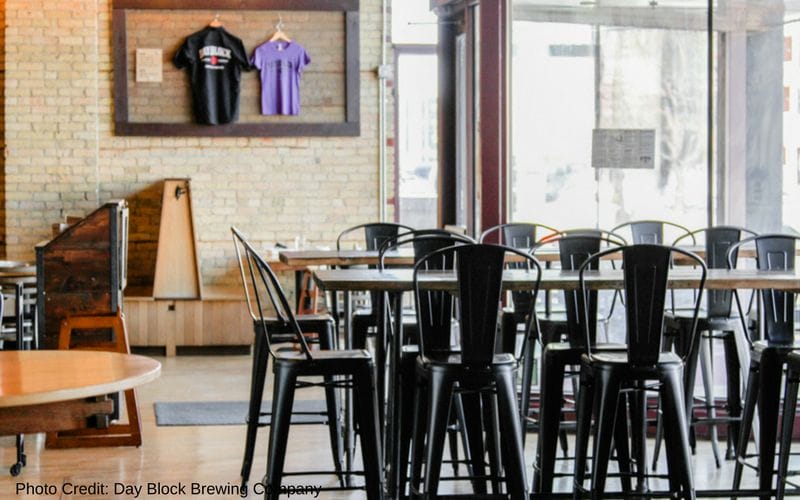 Day Block Brewing Company is one of the best Minneapolis breweries, located in the Mill City neighborhood. Long wooden tables and metal built-in booths inside Day Block Brewing Company's indoor space. The original brick wall is in the background and a wall of windows is letting natural light into the space.