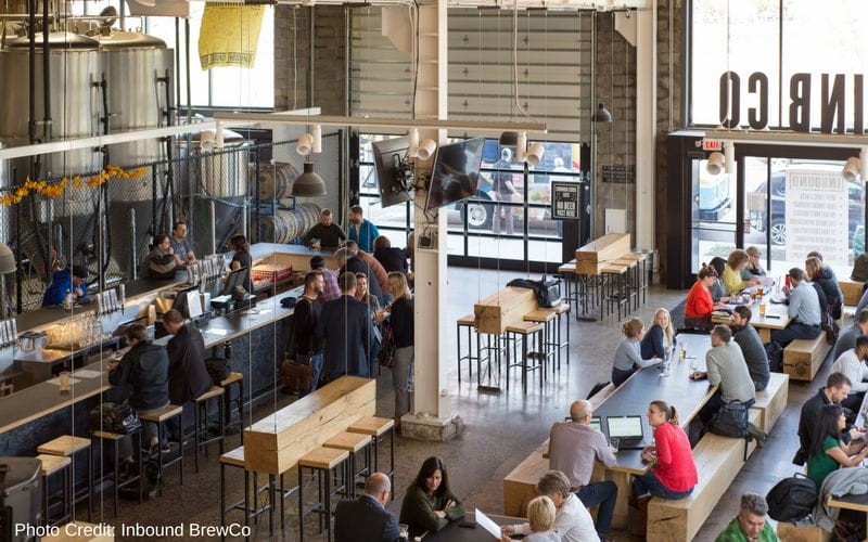 Inbound BrewCo is one of the best Minneapolis breweries, located in the North Loop neighborhood near Target Field. Chunky wood tables and benches filled with people, the metal bar is an island int he center of the space with large metal brewing equipment in the background. The room is lined with windows and doors that open up to the outside.