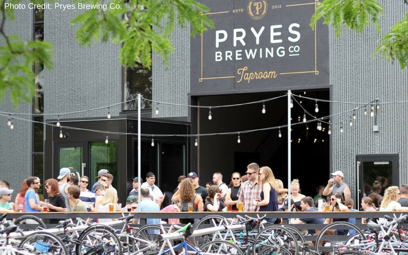 Pryes Brewing Co. is one of the best Minneapolis Breweries, located in the North Loop along the banks of the Mississippi River. An outdoor patio lined with bicycles along the railing in front of a concrete industrial building with a sign reading Pryes Brewing Co Taproom.