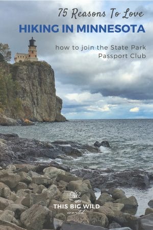A cloudy dramatic sky is the backdrop for Split Rock Lighthouse perched on a tall rocky cliff as seen from the shoreline of Lake Superior below. Text: 75 reasons to love hiking in Minnesota, how to join the Minnesota State Park Passport Club