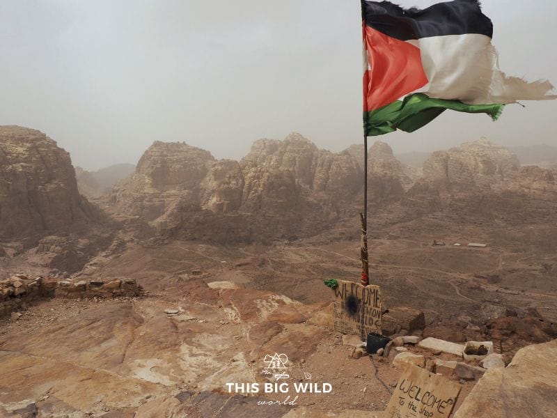Dramatic view during a little windstorm at the High Place of Sacrifice in Petra. The Jordan flag waves in the wind with a view of the trail to the Monastery off in the distance.