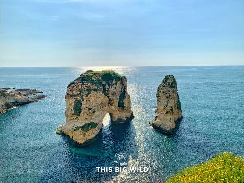 The lightly colored Corniche rock formation standing tall in the bright blue water just before sunset in the Raouche neighborhood of Beirut.
