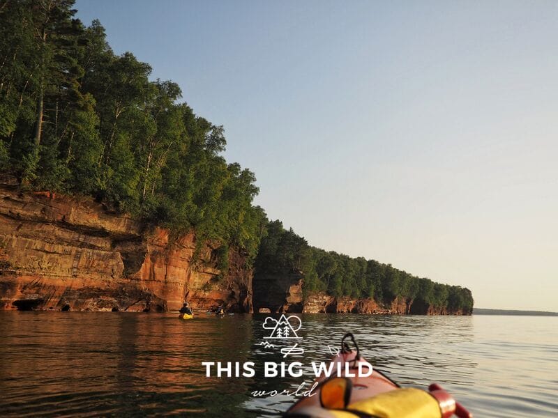 Golden hour, just before sunset, makes the red sandstone change colors creating a dramatic effect from the water while kayaking the Apostle Islands.