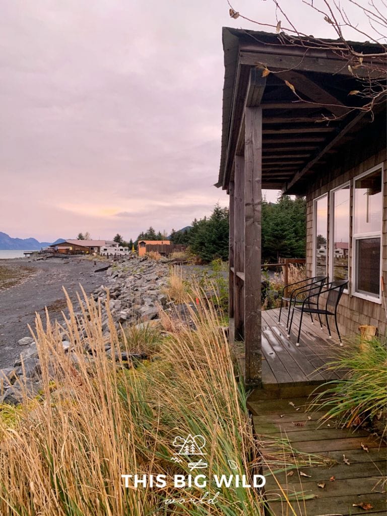 A small cabin with a patio right on the water at Resurrection Bay. The sky is a light pink color with another cabin off in the distance.