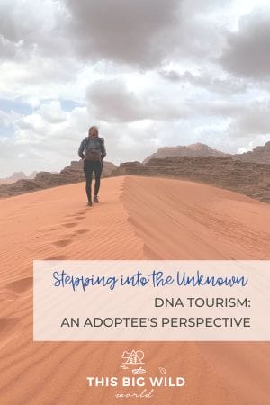 Text: Stepping into the Unknown. DNA Tourism: An Adoptee's Perspective Image: Me walking away from the camera in on a dune made of reddish sand with reddish rock formations and cloudy skies off in the distance.