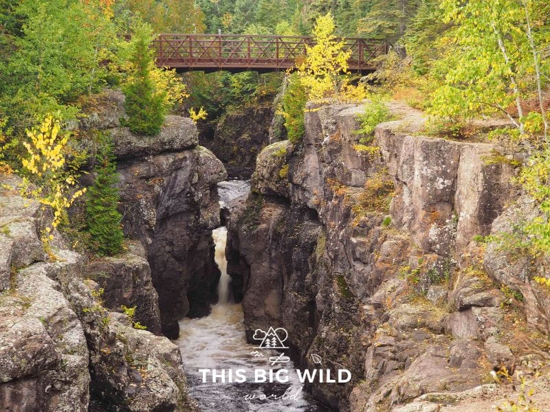 A thin gorge with rushing water runs underneath a red bridge lined with fall colors in Temperance River State Park on the north shore of Lake Superior in Minnesota.