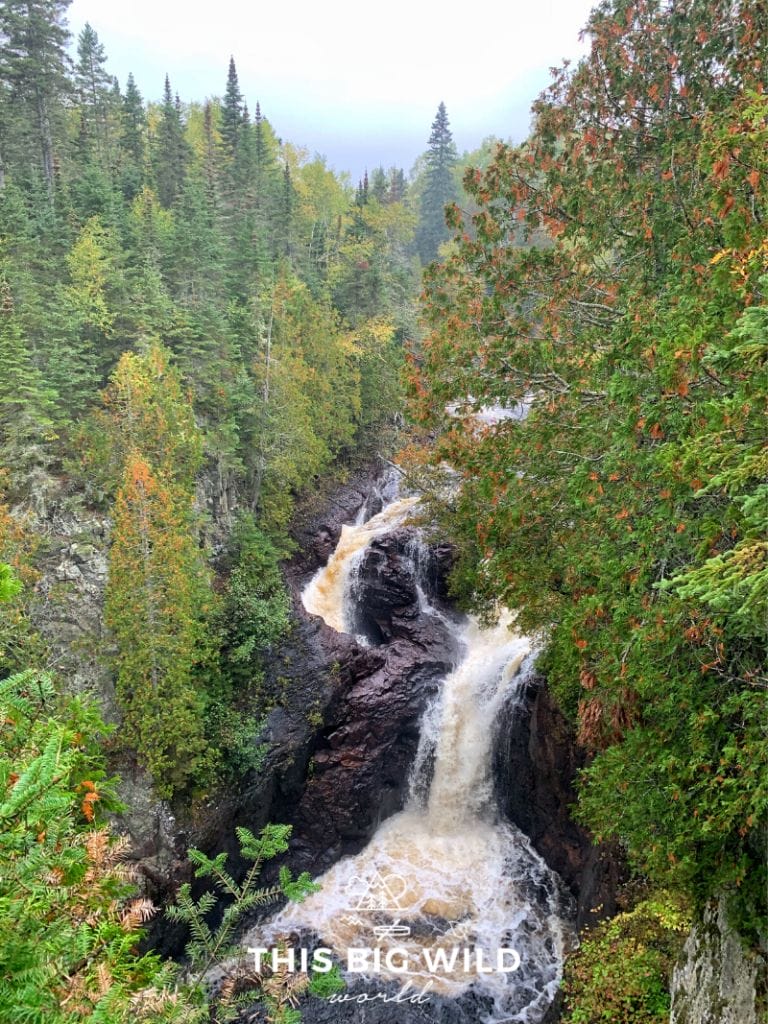 A series of waterfalls flows through dark rock which creates Devil's Kettle Falls in Judge CR Magney State Park in northern Minnesota. The fall colors are just beginning to change creating pops of orange and red in the lush green lining the waterfall. A must for any Minnesota bucket list!
