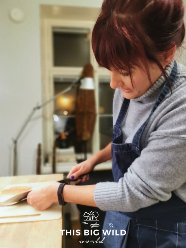 A woman (me) in a gray sweater and denim apron, removing the skin from a salmon fillet for traditional Finnish salmon soup. This was part of an Airbnb Experience in Helsinki Finland.