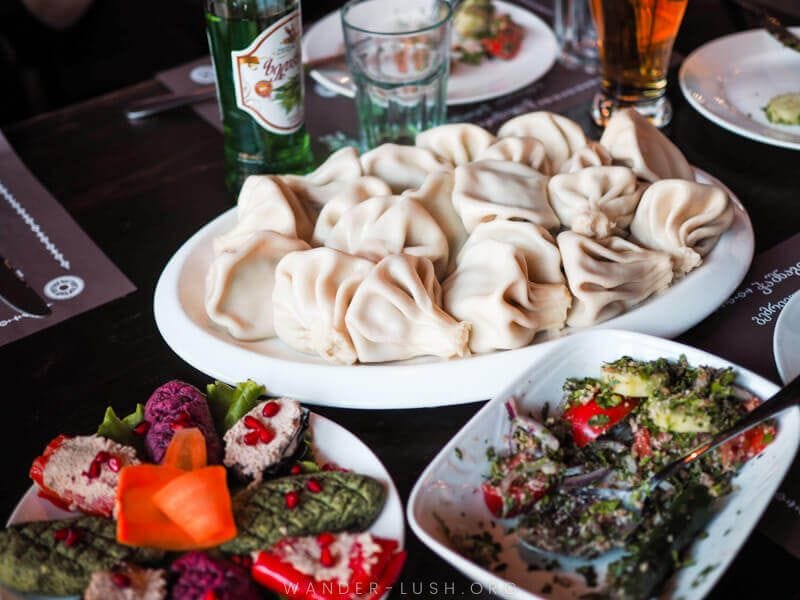 A spread of traditional Georgian foods, including dumplings called Khinkali, on a dark wood table. This was just one stop on Emily's food tour in Tbilisi Georgia. She shares more in this Airbnb Experiences review!