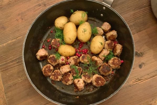 Finnish meatballs and dill potatoes with lingonberries in a metal skillet over a wooden table. Prepared during an Airbnb Experiences cooking class in Helsinki Finland.