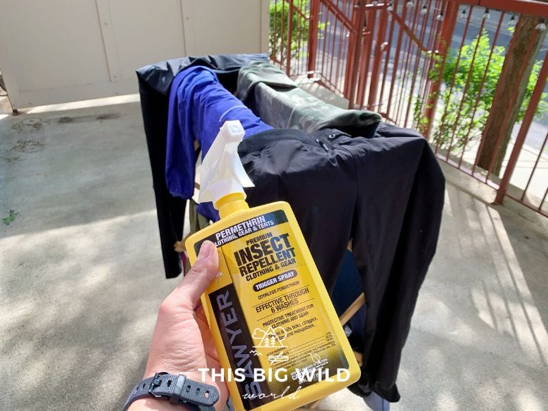 Yellow spray bottle of Sawyer permethrin spray in front of a rack of clothes outside on a patio.