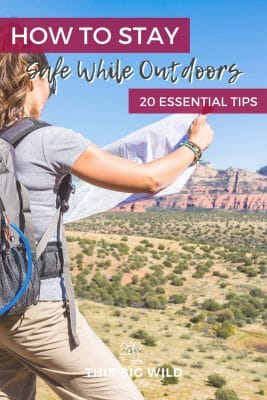 Text: How to Stay Safe While Outdoors - 20 Essential Tips
Image: Women with her back to the camera on the left side of the frame wearing a backpack and holding a map. Behind her is a desert scene with green brush and mountains in the distance.