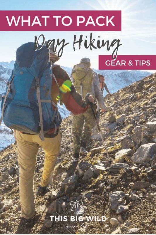 Text: What to Pack Day Hiking Gear & Tips
Image: 3 adults walking away from the camera on a slanted rocky trail with a snow covered mountain in the distance.