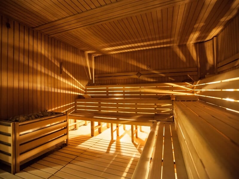 A dimly lit empty wooden sauna is brightened by rays of light coming in through the walls.