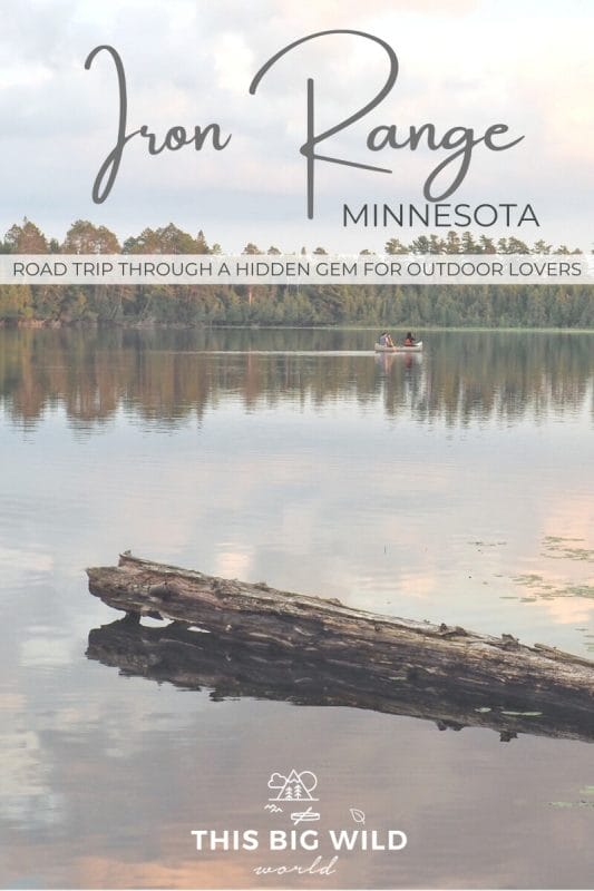 Text: Iron Range Minnesota - Road trip through a hidden gem for outdoor lovers Image: Two people in a canoe paddle away from the camera. A green treeline is in the distance and a log is resting in the water in the foreground.