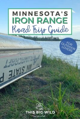 Text: Minnesota's Iron Range Road Trip Guide - for outdoor lovers Image: A metal canoe rests upside down along the shore of a lake in the grass.