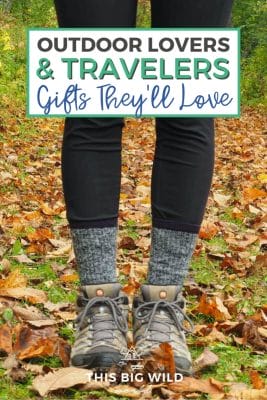 Text: Outdoor Lovers & Travelers - Gifts They'll Love Image: A woman with black leggings and black and white socks in hiking boots stands among fallen autumn leaves.
