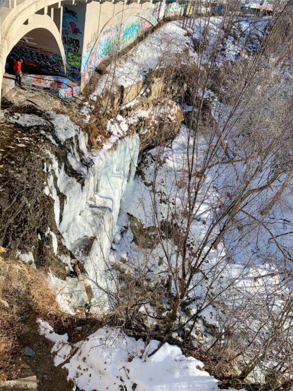 An ice climber reaches the top of Bridal Veil Falls in Minneapolis Minnesota. The frozen waterfall flows under an overpass covered in colorful graffiti before flowing into a ravine towards the nearby Mississippi River.