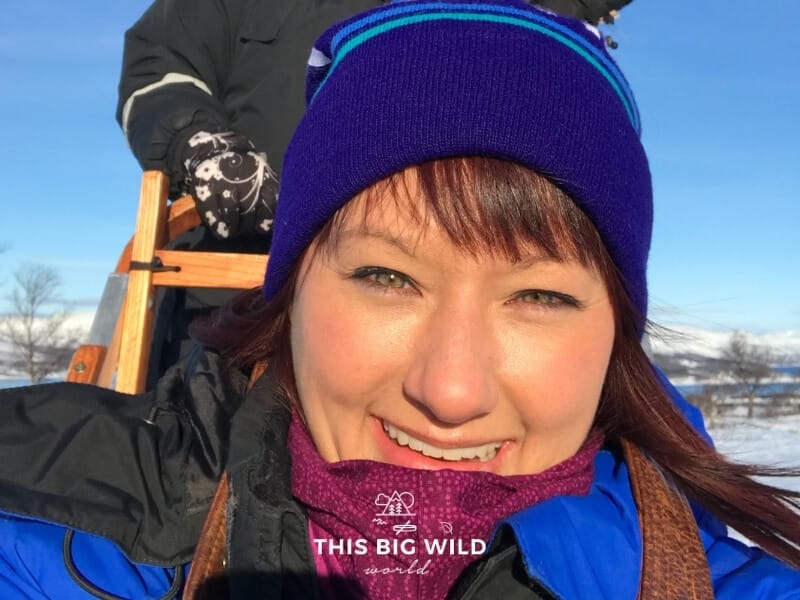 Close up of my face with the sun shining on it because I forgot my sunglasses. I am riding in the sled and another person is behind me driving the sled.