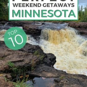 Text: Perfect weekend getaways Minnesota - Top 10 Image: A waterfalls flows over and between dark brown stone lined on either side with green trees and a blue sky overhead.