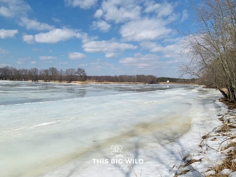 Two iced over rivers merge at Crow Wing State Park under a bright sky with fluffy white clouds.