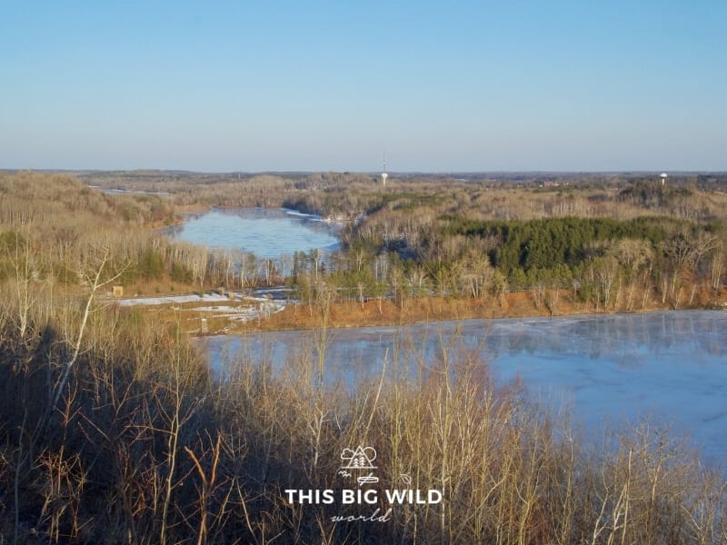 View of 3 different mine pits, now lakes, from the top of Cuyuna Overlook. In winter the mine pits are covered in ice with a hint of snow showing through the trees that extend out to the horizon.