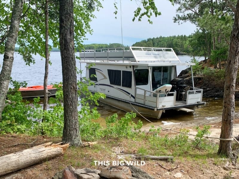 A houseboat is parked on a small stretch of sand surrounded on both sides by a rock. 