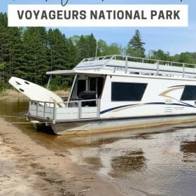 Text: Renting a houseboat Voyageurs National Park Image: Houseboat on a beach with trees behind it.