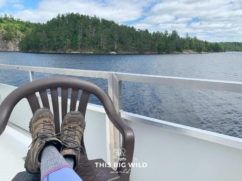A pair of hiking boots rested on a plastic chair on the rooftop of a houseboat overlooking tall cliffs and trees in Voyageurs National Park.