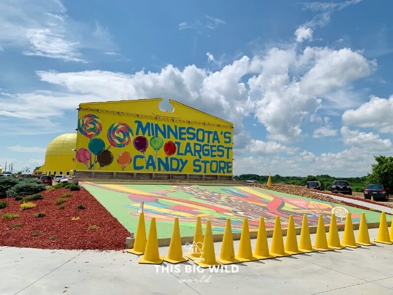 Big yellow sign for Minnesota's Largest Candy Store with a mural painted on the ground in front of it. 
