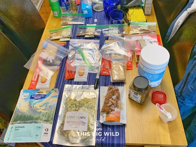 Assorted food is laid on a table with a column for each day. Food items are being repackaged into portions based on calories needed each day.
