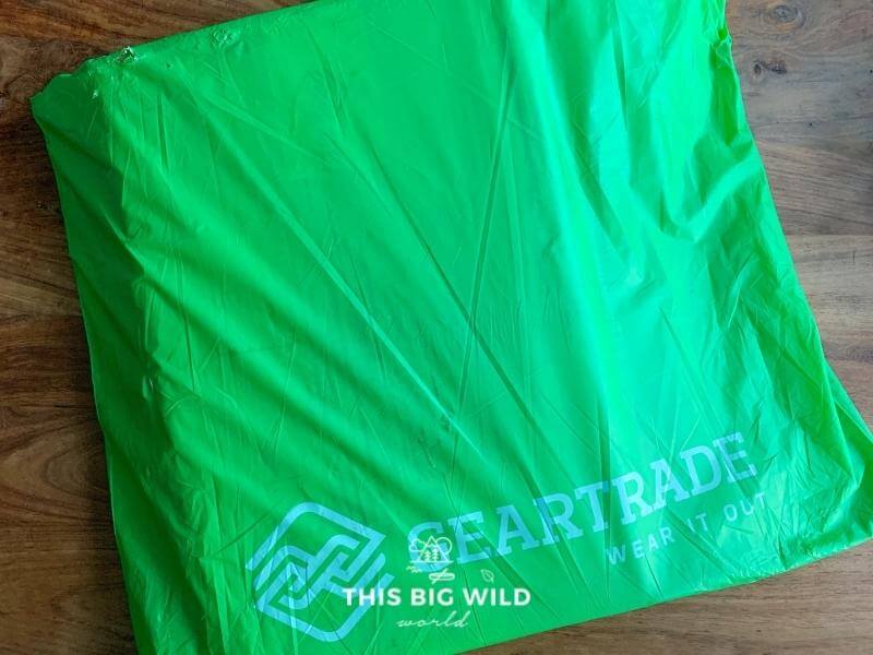 Green mailing envelope from Geartrade on a wooden table. The envelope contains a prepaid shipping label and box to send used outdoor gear to them to sell for you!