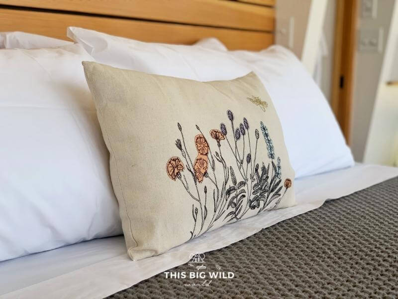 Closeup of the bedding at Nordlys Airbnb has embroidered floral detail on a linen pillow and crisp white sheets.