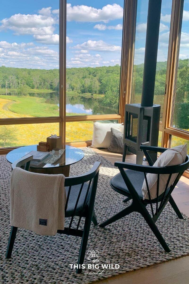 Two chairs next to a fireplace look out a wall of windows to a field of wildflowers at Nordlys in Wisconsin.