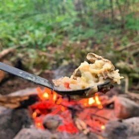 Spoon of food being held up in front of a campfire - dehydrating your own backpacking meals for beginners!