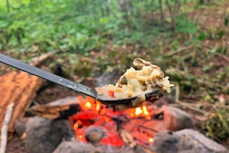 Spoon of food being held up in front of a campfire - dehydrating your own backpacking meals for beginners!