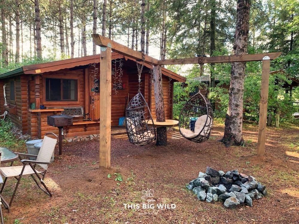 The view of The Timberjack cabin in Hayward Wisconsin, with the outdoor space, fire pit and hanging chairs.