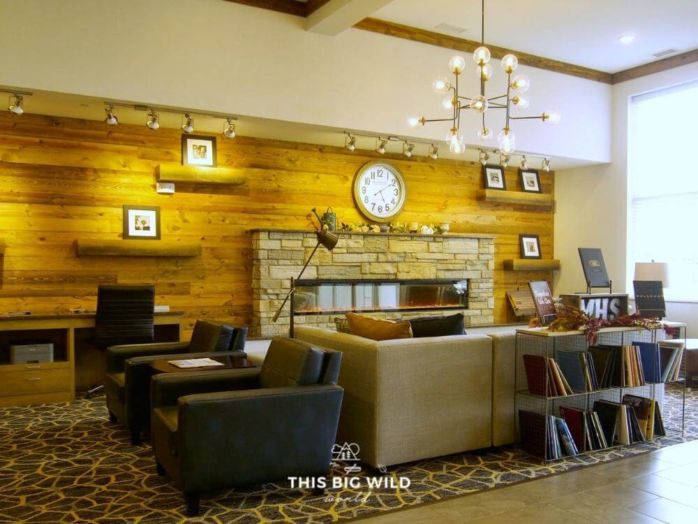 Distressed wood along the wall with a fireplace, comfy couches and chairs and modern lighting in the GrandStay Milbank lobby.