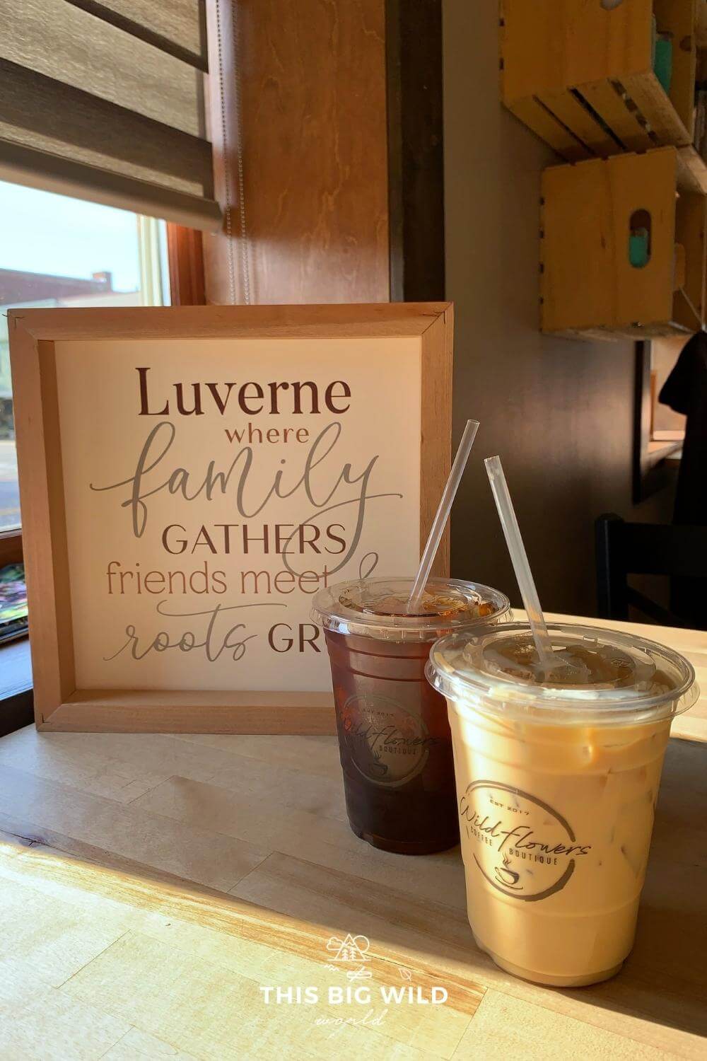 Two iced coffees next to a sign that says "Luverne where family gathers friends meet roots grow"