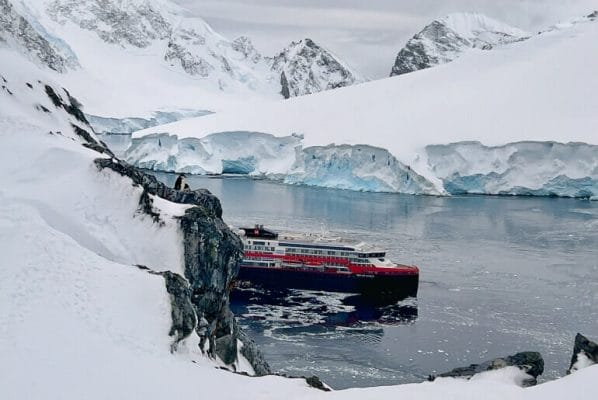 MS Fridtjof Nansen in a harbor in Antarctica with chinstrap penguins in the foreground.