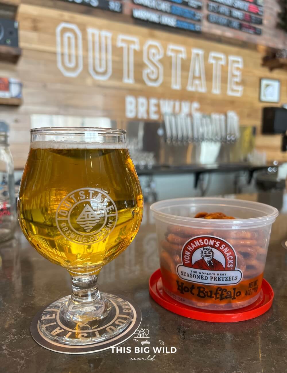 Glass of IPA next to a container of pretzels on the bar at Outstate Brewing.