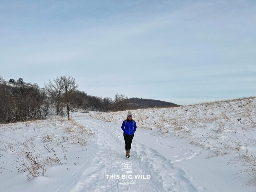 Me hiking the Hallaway Hill trail at Maplewood State Park in the snow, with prairie and hills on both sides of the trail.