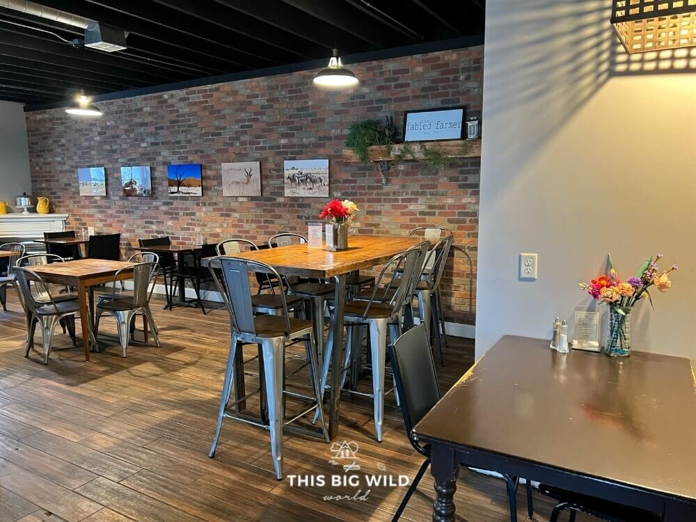 Interior of The Fabled Farmer has a brick wall, wood floor, metal chairs for a farmhouse feel.