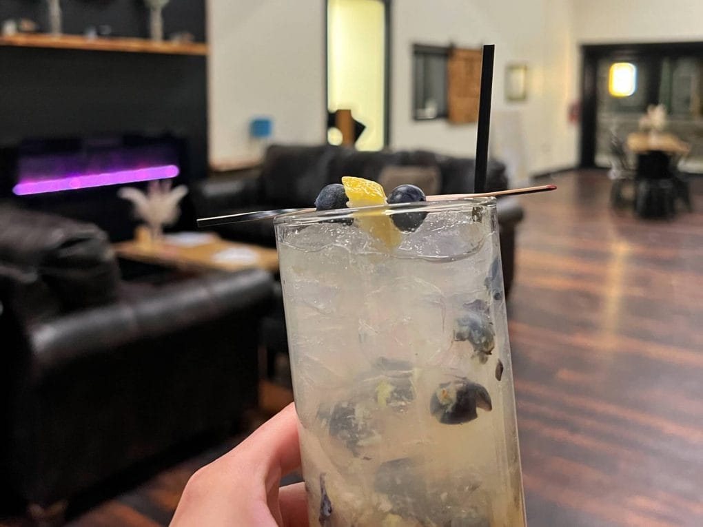 Cocktail being held up in front of sofas and a fireplace in a distillery tasting room.