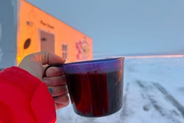 Cup of coffee in front of an ice fishing sleeper house on Lake of the Woods at sunrise