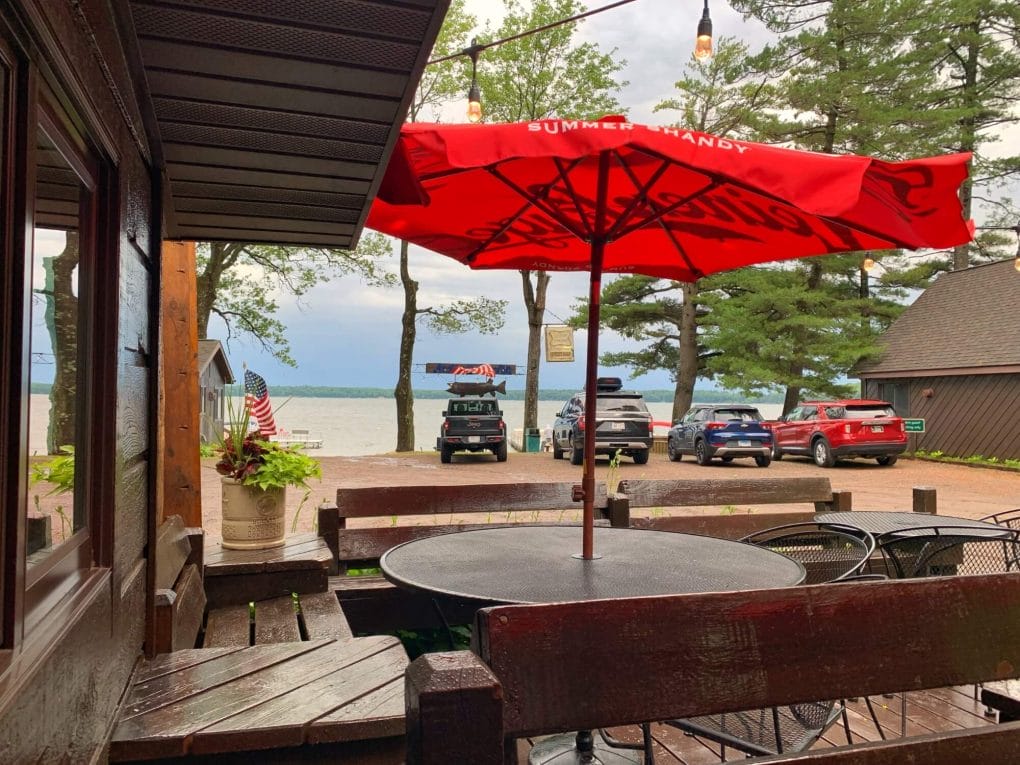 Outdoor patio with wooden seating, red umbrella and lake in the distance