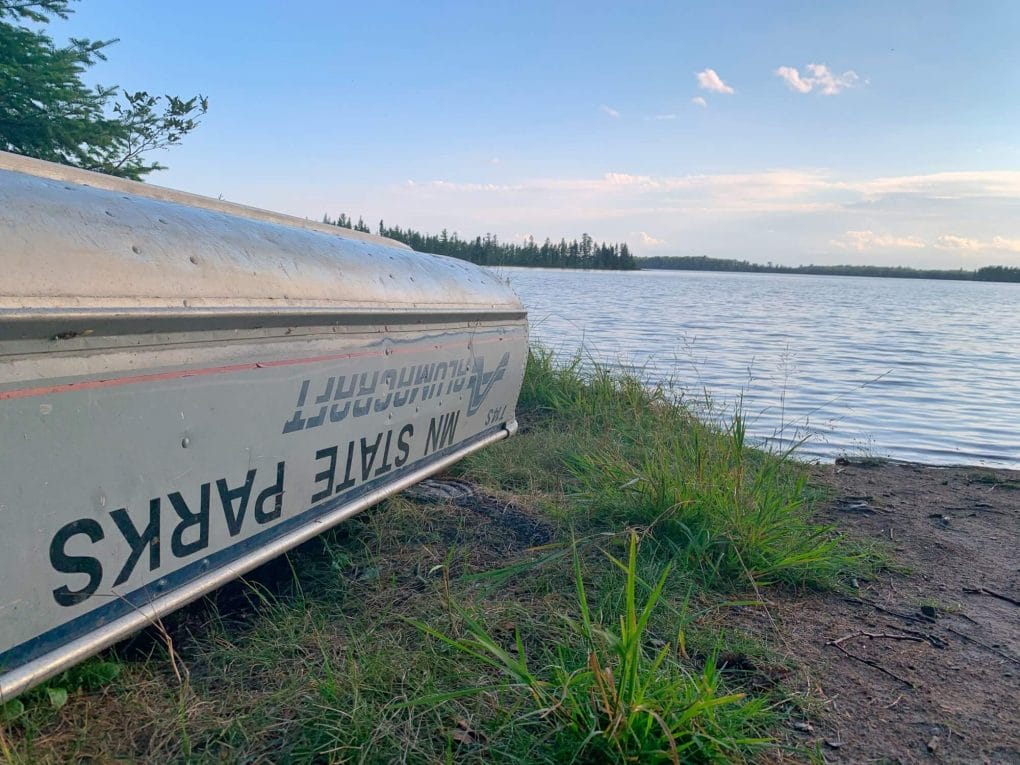 A metal row boat upside down next to a lake in a Minnesota State Park.